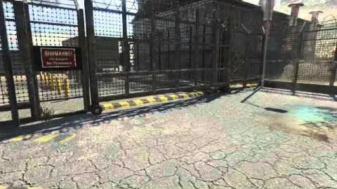 A chain-link compound gate with a warning sign beside it, empty cracked tarmac in front.