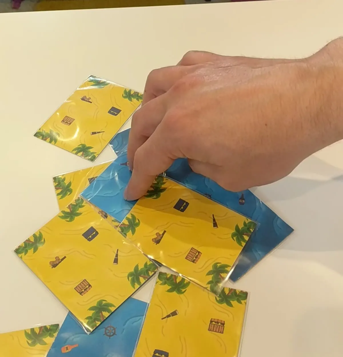 A hand with one finger pinned on a card in the middle of a heap of sleeved cards on a white table, rotating it