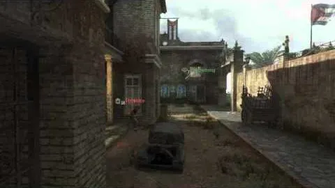 A narrow courtyard between brick buildings, a burnt-out car in the middle and two tagged players further down the street.